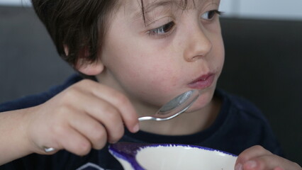 Small boy eating cereal with spoon inside bowl. Candid hungry child snacking wheat food for...