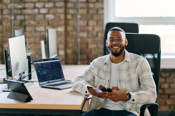  African American entrepreneur takes a break in a modern office, using a smartphone to browse...