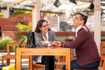 Happy young Latin couple in love holding hands waiting at a table in a restaurant or cafeteria.