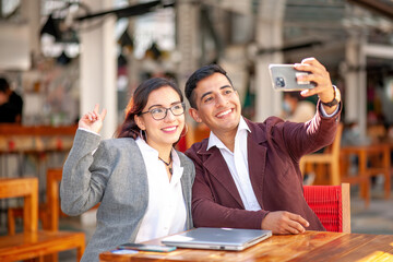 Portrait of young Latinos taking a selfie with their cell phone at a restaurant table.