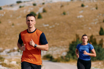 Fototapeta premium A couple dressed in sportswear runs along a scenic road during an early morning workout, enjoying the fresh air and maintaining a healthy lifestyle