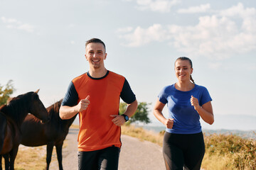 A couple dressed in sportswear runs along a scenic road during an early morning workout, enjoying...