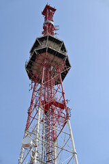 Red and white communication tower against blue sky