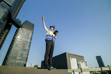 Skilled engineer operating tablet to manage HVAC machinery on top of building, urban architecture in distance.