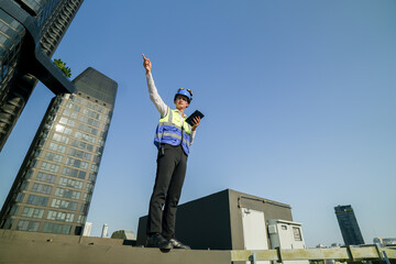 Skilled engineer operating tablet to manage HVAC machinery on top of building, urban architecture in distance.