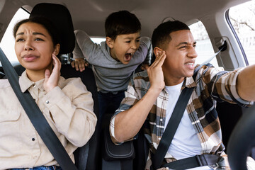 Preteen boy shouting, feeling angry, parents covering ears while travelling together by car, having family conflicts during car trip