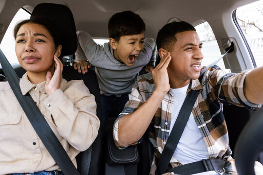 Preteen boy shouting, feeling angry, parents covering ears while travelling together by car, having family conflicts during car trip - Powered by Adobe