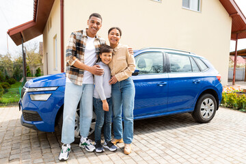 Happy family with their son arrived by car to their new home, posing and embracing. Renting and...