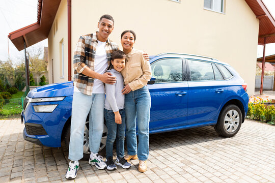 Happy family with their son arrived by car to their new home, posing and embracing. Renting and buying house