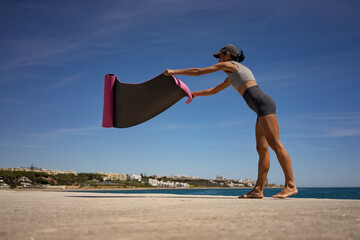 Athletic Brunette Woman Elegantly Unfolds Pink Exercise Mat on Seashore by the Ocean