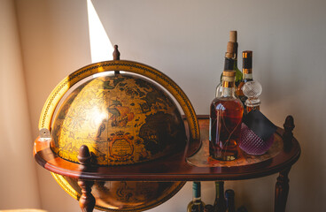 Vintage voyages: old terrestrial globe in a classic wooden bar station adorned with antique alcohol bottles