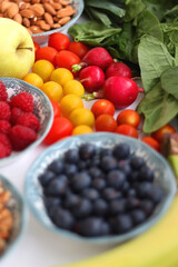 Apples, lemons, bananas, berries, carrots, leek, tomatoes, radishes, spinach and various nuts on white background. Healthy seasonal fruit and vegetable. Selective focus.