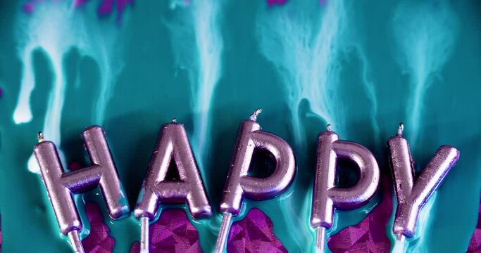 Happy birthday. Festive font. Ink spill. Metallic shiny letter candles in iridescent glow light with blue white color paint fluid drip flow on pink surface abstract art background.