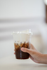 hand of woman holding a take-out iced espresso with cream foam at cafe, isolate concept.	