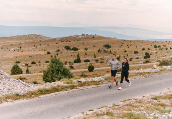 A couple dressed in sportswear runs along a scenic road during an early morning workout, enjoying the fresh air and maintaining a healthy lifestyle