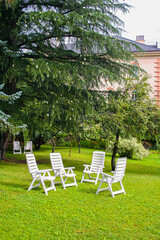 Six white chairs on green grass in a garden..