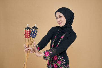Beautiful Asian model wearing black kebaya dress with hijab, holding a bamboo torch over beige...