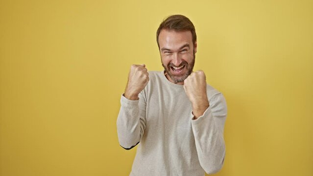 Joyful middle-aged hispanic man screaming in celebration, standing exalted with a winning gesture on a yellow isolated background, overflowing with excitement and success