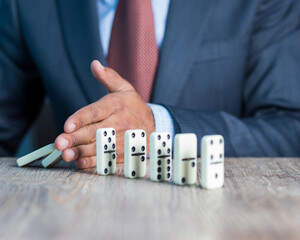 Business man stoping domino effect by his hand, business strategy background image, wearing blue...