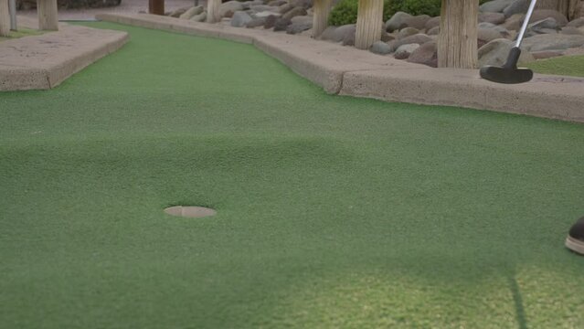 This video shows a slow motion side view of a red golf ball being putted into a miniature golf course hole.