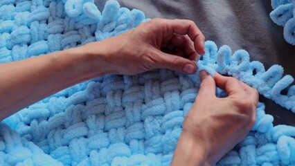 A woman lovingly crafts a blue blanket for her grandson with her own hands, each stitch a testament to her care and devotion. Create cherished memories with handmade treasures.