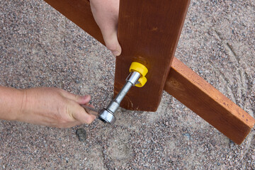 Ratchet socket wrench tightens bolt when assembling wooden outdoor furniture.