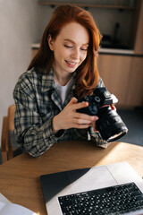 Vertical portrait of young female photographer holding modern digital camera looking at screen...