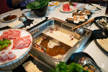 A square-sized Chinese hotpot bubbles with savory broth, inviting diners to enjoy a ready-to-eat steamboat experience in the restaurant. - obrazy, fototapety, plakaty