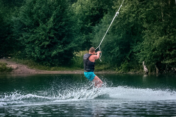 A man wakeboarding on a lake on summer day in a life  jacket. Soft focus. Action blur.