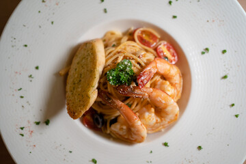 Top-down view of flavorful tomato pasta with prawns, accompanied by bread and cherry tomatoes.