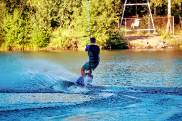 A man wakeboarding on a lake on summer day in a life  jacket. Soft focus. Action blur.