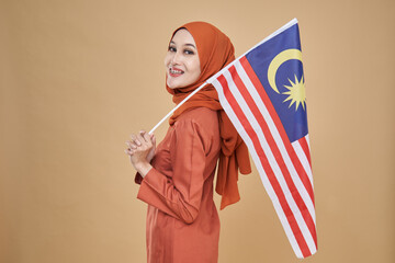 	
Beautiful Asian girl wearing traditional kebaya with hijab, happily holding Malaysian flag isolated over beige background. Independence day, new year nationalism concept