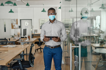 African businessman wearing a face mask working on a tablet