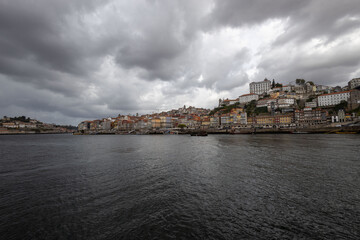 View of the north bank of the Duero River in Porto west of the Luis I Bridge from river level with wide angle objects - Bishop's Palace - cumulus clouds - obrazy, fototapety, plakaty