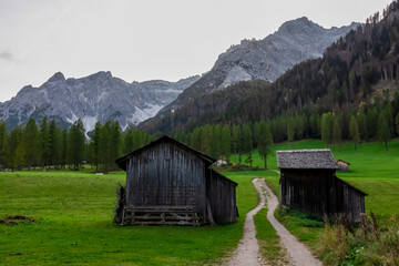 Scenic hiking trail along wooden huts on idyllic alpine meadow with awe view of majestic mountain peaks of Sexten Dolomites, South Tyrol, Italy, Europe. Hiking in panoramic Fischleintal, Italian Alps - obrazy, fototapety, plakaty