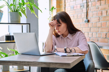 Mature tired worried tense woman at workplace experiencing stress headache