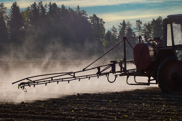 An aerosol cloud behind farm tractor spraying herbicides in potato field.