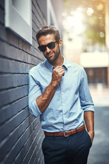 Sunglasses, fashion and man by brick wall in city with trendy, stylish and classy outfit. Accessory, handsome and male public relations officer with elegant shirt and pants with confidence in town.