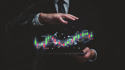 A man is holding a tablet with a candlestick line graph and chart. The graph is showing a stock...