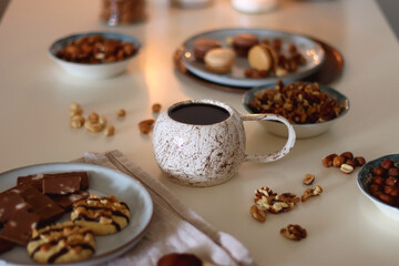 Cup of tea or coffee, cookies, macaroons, chocolate, various nuts and cocoa powder on white background. Selective focus.