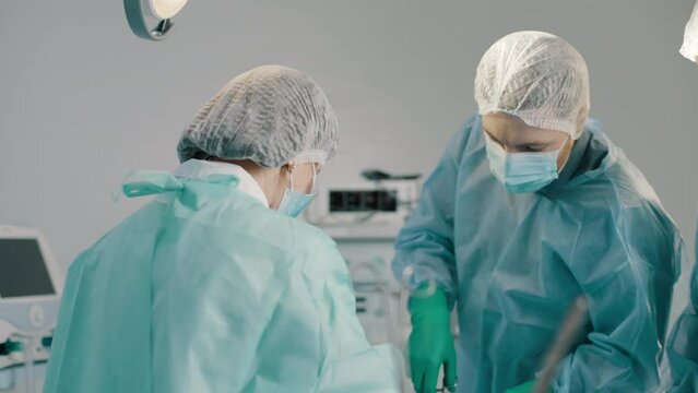 Team of professional surgeons performs surgery on patient under anesthesia in operating room. A nurse hands a medical instrument to a doctor