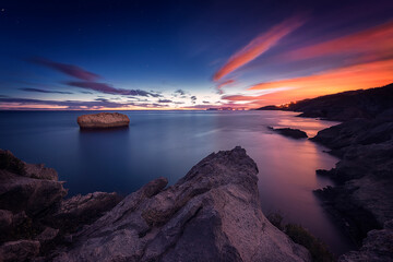 Warm sunrise in Islares, Cantabria, with a close-up of rocks and a rock in the middle of the sea