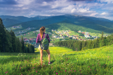Girl on the hill with yellow flowers and green grass in beautiful alpine mountain valley at sunset in summer. Landscape with young woman in alps, trees, sky with clouds. Hiking. Spring in Europe - 787501144