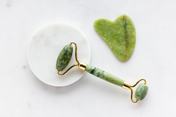 Green jade roller massager for face on white marble.