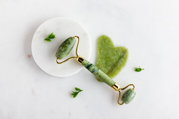 Green jade roller massager for face on white marble.