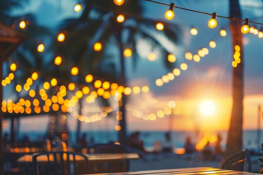 blurred bokeh light on sunset with yellow string lights decor in beach restaurant.