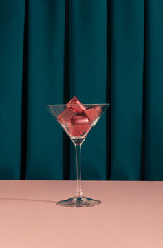Creative arrangement of martini glass filled with chocolate candies in pink foil. Elegant scene with a green curtain in the background.