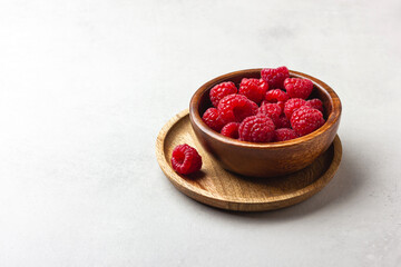 Fresh raspberries in a wooden bowl on a light grey background