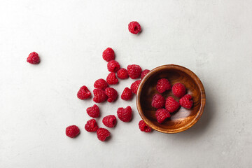 Fresh raspberries in a wooden bowl on a light grey background