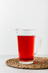 Red color drink in the glass jug on gray background.
